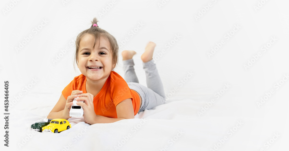 Little girl playing with white toy car. Sitting on the white bedsheet. Smiling. Little girl playing with white toy car. Sitting on the white bedsheet. Smiling.