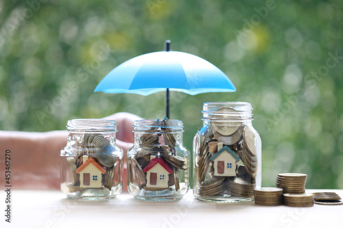 Protection,Model house and gold coin money in the glass bottle with hand holding the umbrella on natural green background, Finance insurance and Safe investment concept