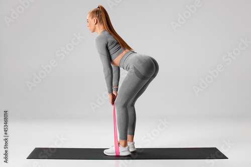 Athletic girl doing deadlift exercise for glutes with resistance band on gray background. Fitness woman working out photo