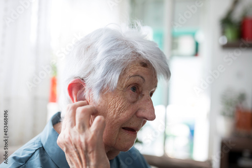 Close up of serious senior gray-haired Caucasian woman adjusting her in-ear hearing aid kit