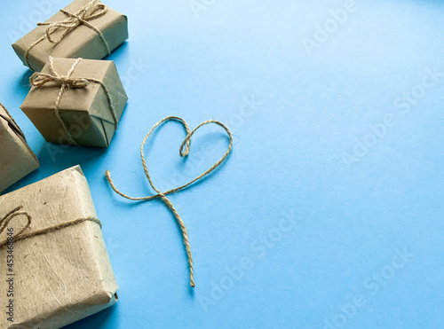 Gift wrapping in kraft paper with a heart made of threads on a blue background. Minimalism. The concept of the holiday, love, birthday. Place for text, romantic wallpaper. Flat lay, top view