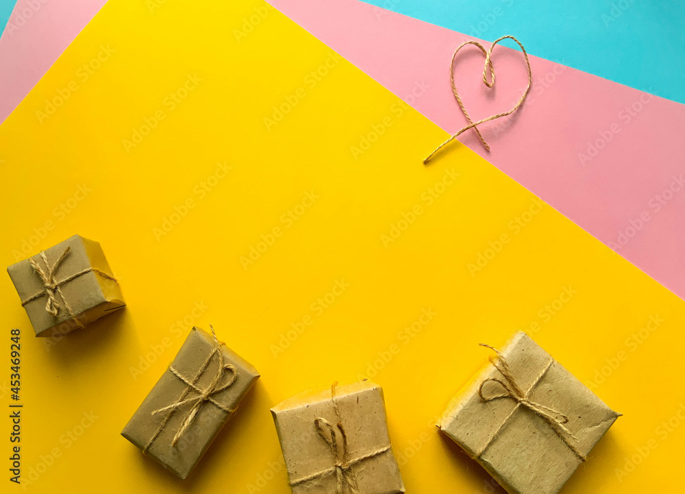 Gift wrapping in kraft paper with a heart made of threads on bright colorful background. Minimalism. The concept of the holiday, love, birthday. Place for text, romantic wallpaper. Flat lay, top view Gift wrapping in kraft paper with a heart made of threads on bright colorful background. Minimalism. The concept of the holiday, love, birthday. Place for text, romantic wallpaper. Flat lay, top view