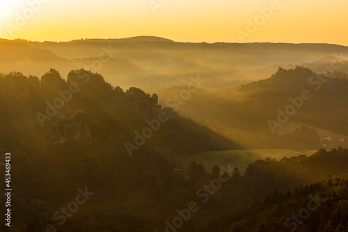 Morning sun shining through foggy landscape with rocks and forest.