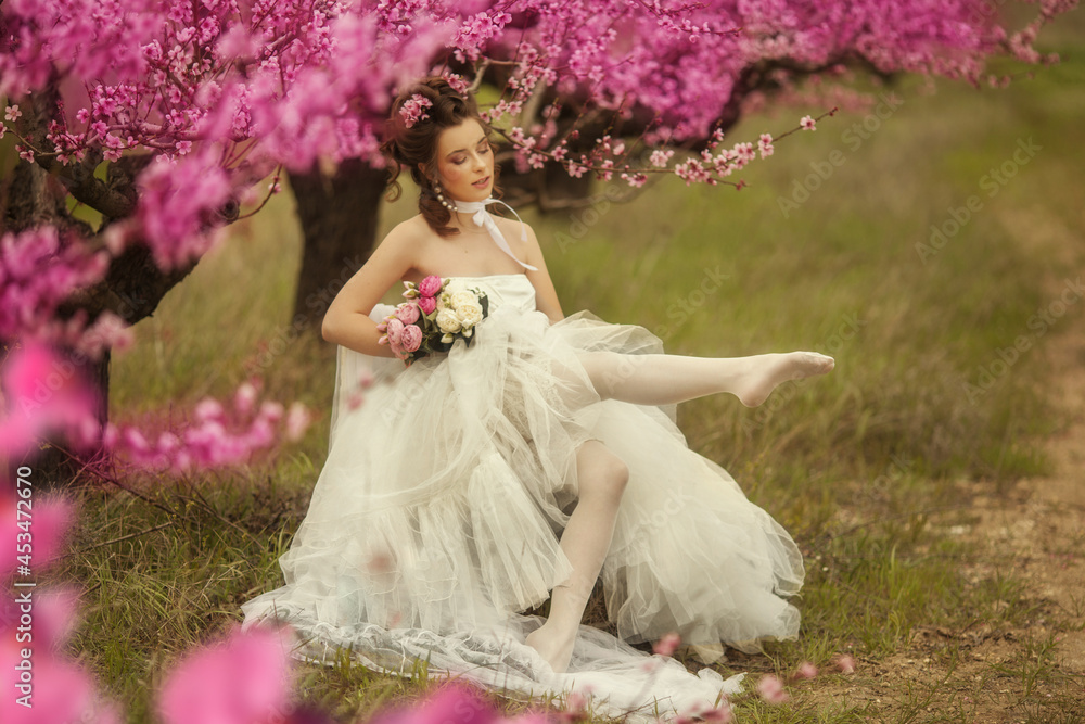 Beautiful bride in a white dress under the sakura tree and flower petals 