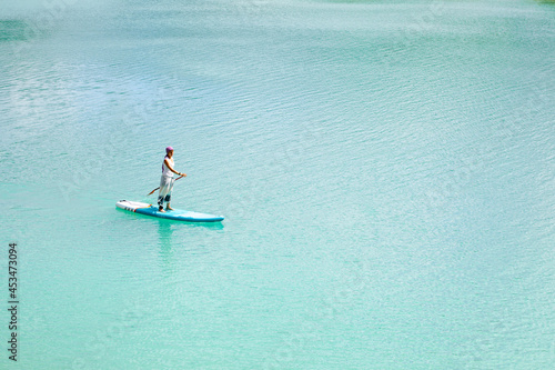 A girl in a dress floats on a glanders board on a pond with bright turquoise water. Warm summer day for travel.  © Sergei Malkov