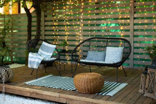 Terrace house with plants, wooden wall and table, comfortable sofa, armchair and lanterns Fototapeta