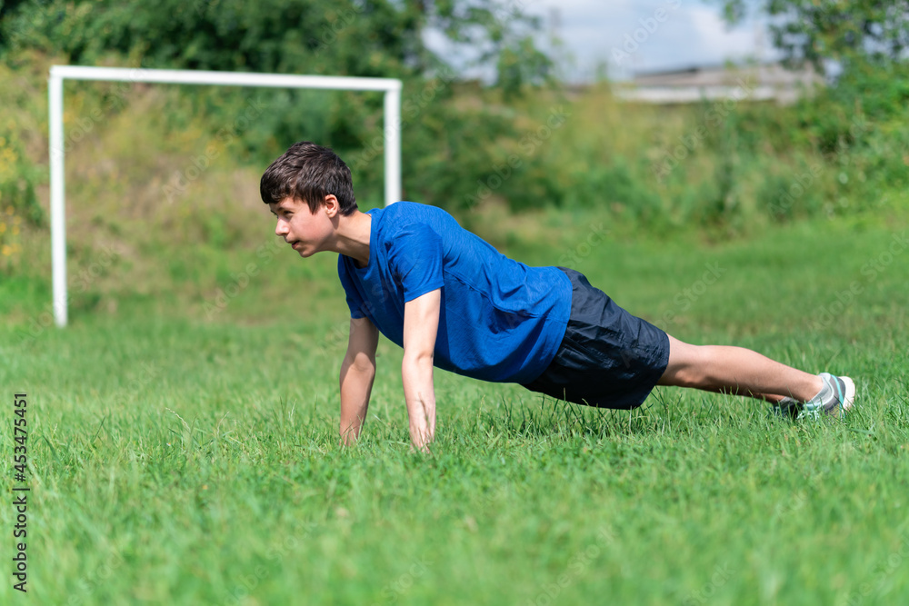 teenage boy exercising outdoors, sports ground in the yard, he does push-ups on the soccer field, healthy lifestyle teenage boy exercising outdoors, sports ground in the yard, he does push-ups on the soccer field, healthy lifestyle