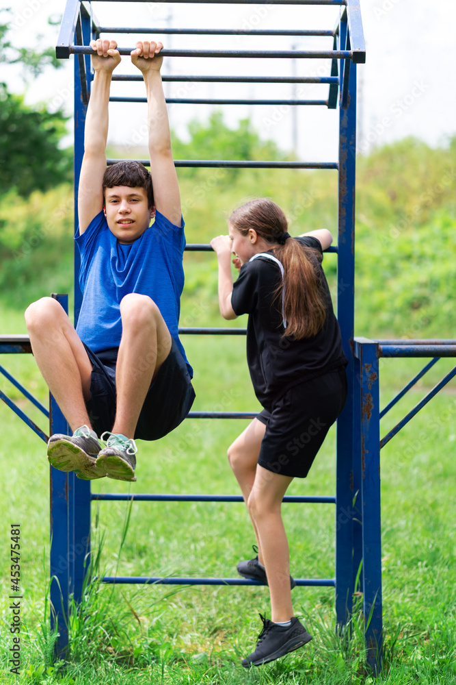 Obraz premium teenage boy and girl exercising outdoors, sports ground in the yard, they posing at the horizontal bar, healthy lifestyle