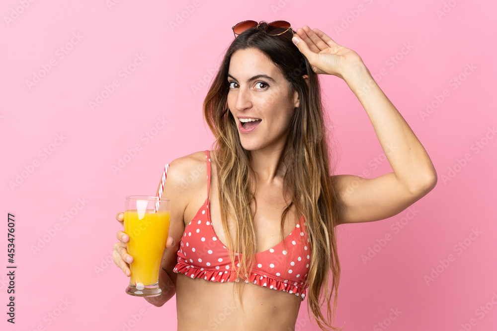 Naklejka premium Young blonde woman over isolated pink background in swimsuit and holding a cocktail