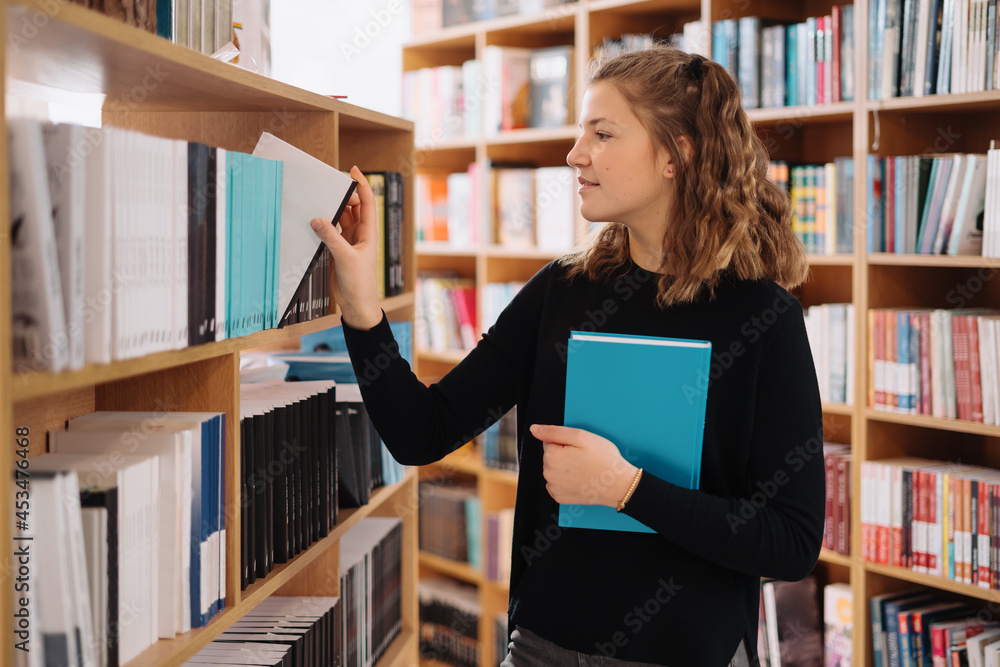 Happy tenage girl or student taking book from shelf in library - People, knowledge, education and school concept Happy tenage girl or student taking book from shelf in library - People, knowledge, education and school concept