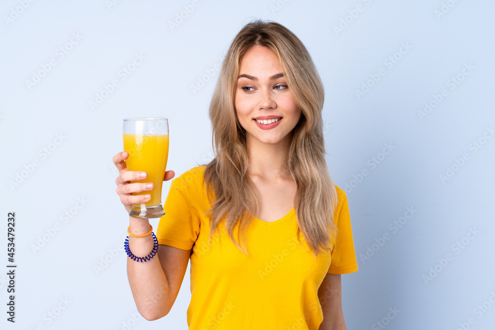 Teenager Russian girl holding an orange juice isolated on blue background with happy expression Teenager Russian girl holding an orange juice isolated on blue background with happy expression