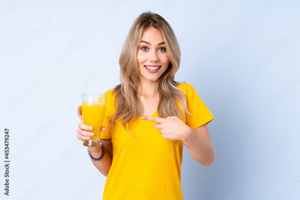 Teenager Russian girl holding an orange juice isolated on blue background with surprise facial expression Teenager Russian girl holding an orange juice isolated on blue background with surprise facial expression