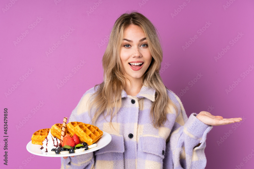 Teenager Russian girl holding waffles isolated on purple background with shocked facial expression Teenager Russian girl holding waffles isolated on purple background with shocked facial expression