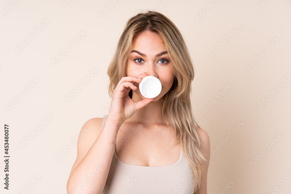 Teenager blonde girl with moisturizer over isolated background Teenager blonde girl with moisturizer over isolated background