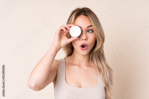 Teenager blonde girl with moisturizer over isolated background