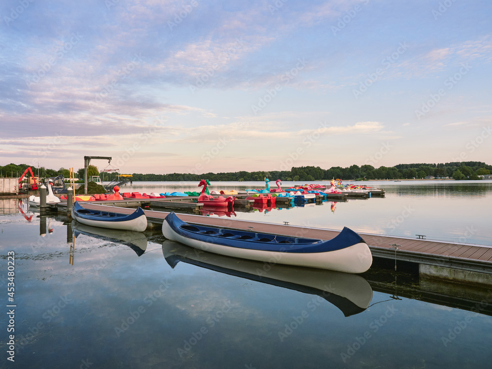 Fototapeta premium A quiet evening at Lake Unterbacher See in German city of Dusseldorf. Moored pedalos nad kayaks for rent. Beautiful landscape before the sunset