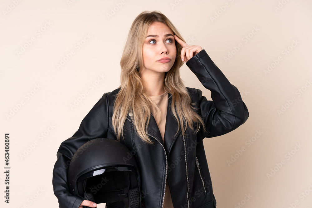 Russian girl with a motorcycle helmet isolated on beige background having doubts and thinking Russian girl with a motorcycle helmet isolated on beige background having doubts and thinking