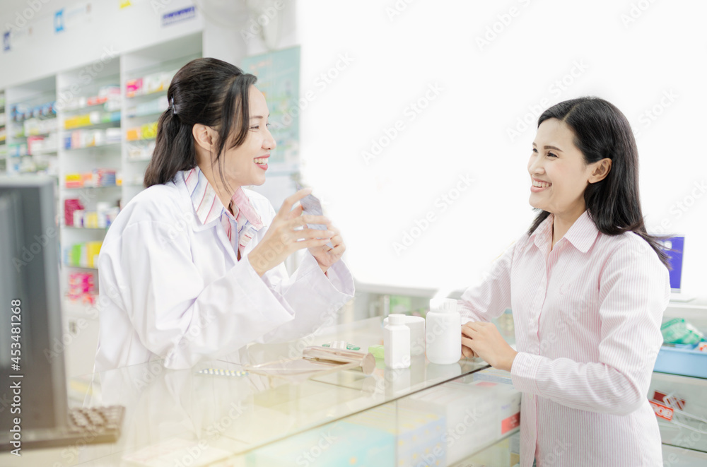 asian female pharmacist explain about how to use drug, she holding drug strip pack with her hand and talk with customer in drugstore asian female pharmacist explain about how to use drug, she holding drug strip pack with her hand and talk with customer in drugstore