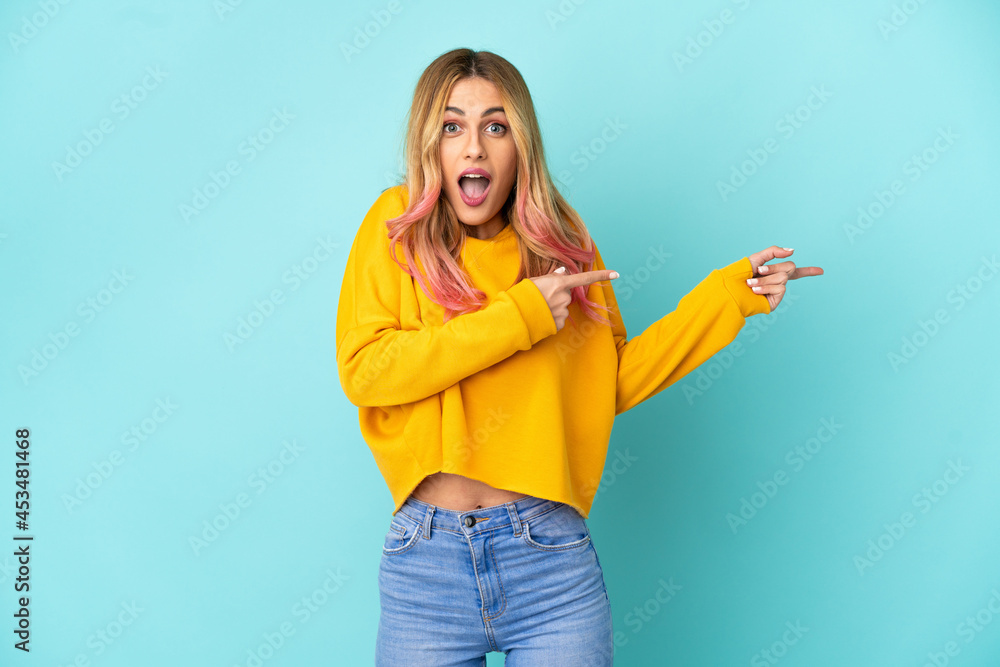Young woman over isolated blue background surprised and pointing side Young woman over isolated blue background surprised and pointing side