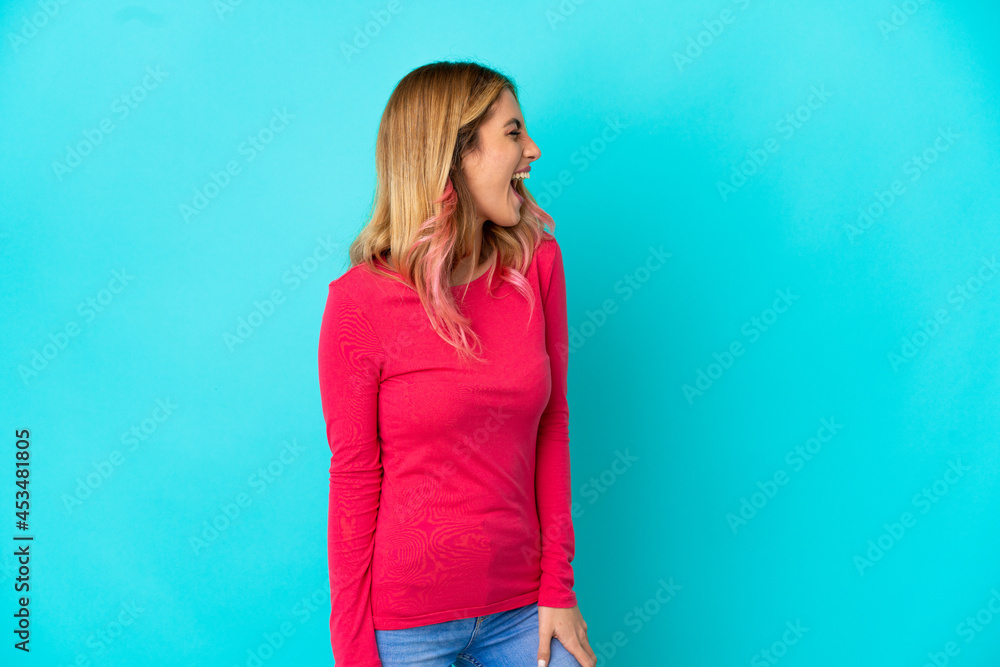 Young woman over isolated blue background laughing in lateral position Young woman over isolated blue background laughing in lateral position