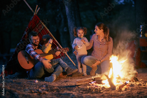 A young couple and children enjoying a campfire and a guitar in the forest