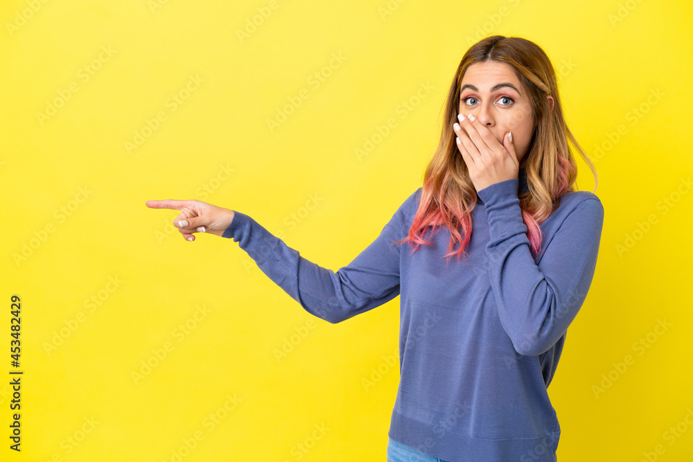 Young woman over isolated yellow background with surprise expression while pointing side Young woman over isolated yellow background with surprise expression while pointing side