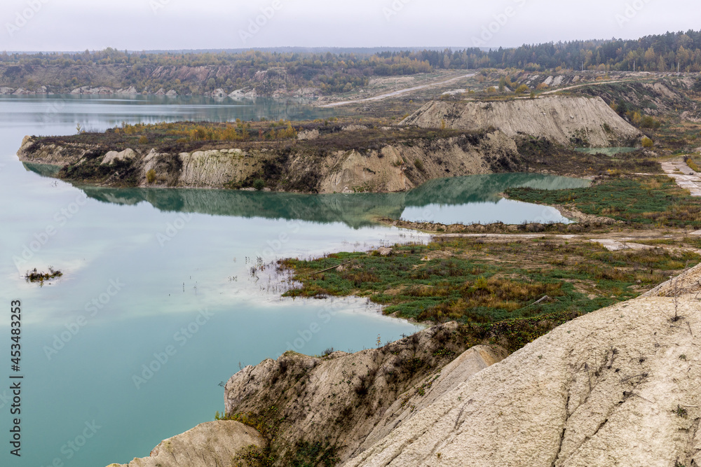 Turquoise water in a chalk quarry in Krichev Belarus. Extraction of chalk. Cretaceous quarries against the background of an autumnal forest of green and yellow color with hillocks from reclaimed earth