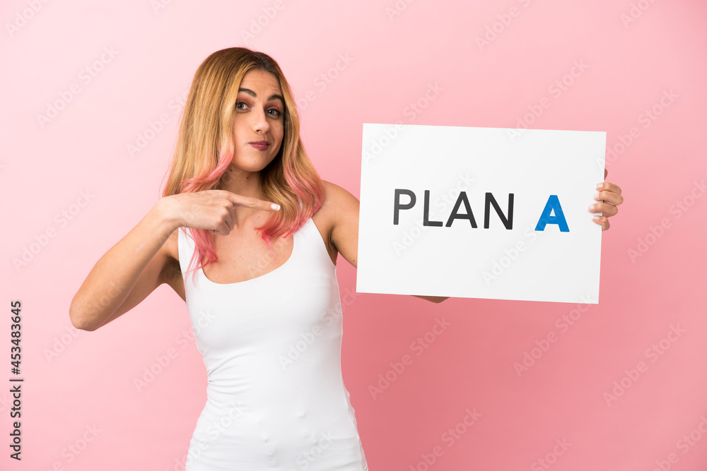Young woman over isolated pink background holding a placard with the message PLAN A and pointing it Young woman over isolated pink background holding a placard with the message PLAN A and pointing it
