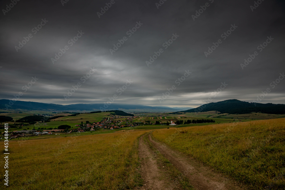 Dirt road leading to a small hungarian village in Transylvania Romania, dark thick rain clouds in the background. Dirt road leading to a small hungarian village in Transylvania Romania, dark thick rain clouds in the background.