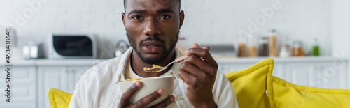 young african american man holding bowl with corn flakes and spoon  banner