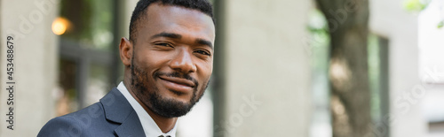 smiling african american businessman in suit looking at camera outside, banner