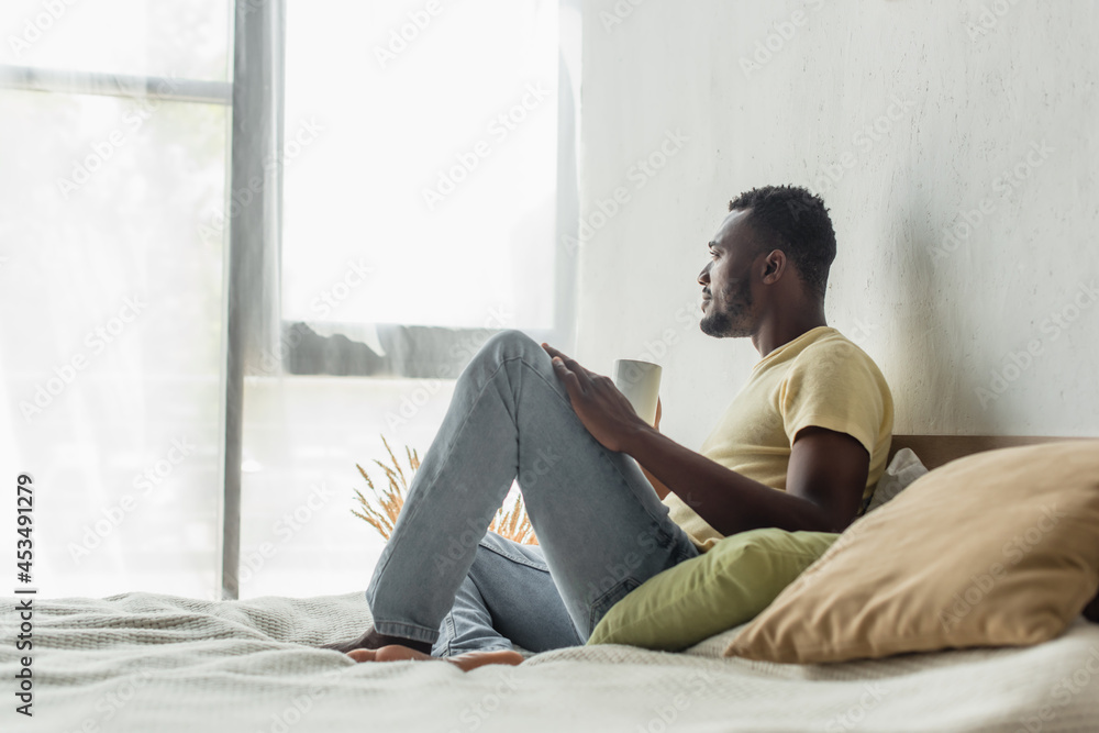 side view of african american man holding cup of coffee in bed