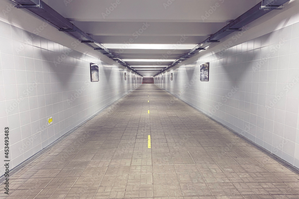 Underground pedestrian crossing in the city illuminated by artificial white light. Stairs at the end of the tunnel. Road separation, traffic direction due to Covid. Pedestrian crossing in the metro.