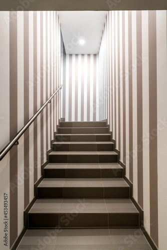 Vertical shot of gloomy lit staircase with vertical dark and white stripes on the walls. Concept for maze  labyrinth  mystery  secret chamber.