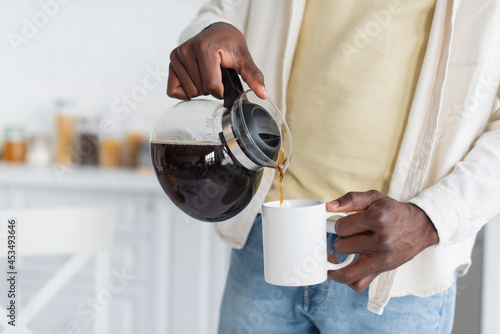 Fotografie cropped view of african american man holding coffee pot and pouring drink in cup