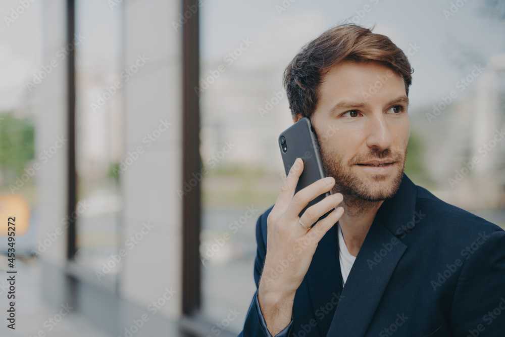 Pensive male entrepreneur focused into distance makes answering call uses mobile phone Pensive male entrepreneur focused into distance makes answering call uses mobile phone