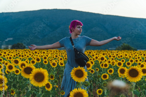 mujer de cabello rosa con los brazos abiertos en medio de un campo de girasoles, mujer con riñonera junto a muchos girasoles, niña feliz en medio de girasoles gigantes photo