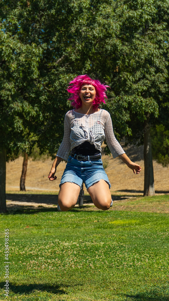 MUJER DE PELO ROSA SALTANDO EN EL PARQUE, MUJER FELIZ SUSPENDIDA EN EL AIRE, MUJER EN BLUSA BLANCA Y PANTALONES CORTOS AZULES SALTANDO MUY FELIZ MUJER DE PELO ROSA SALTANDO EN EL PARQUE, MUJER FELIZ SUSPENDIDA EN EL AIRE, MUJER EN BLUSA BLANCA Y PANTALONES CORTOS AZULES SALTANDO MUY FELIZ