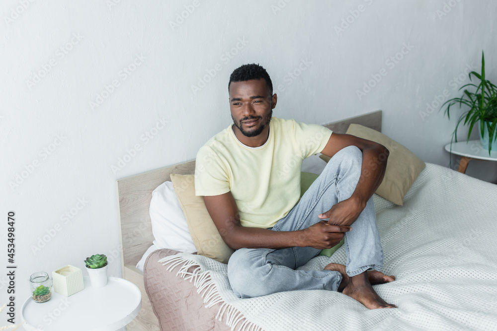 barefoot african american man looking away while sitting on bed barefoot african american man looking away while sitting on bed