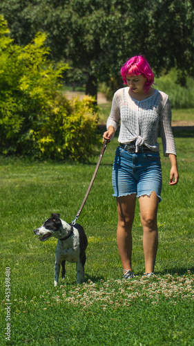 Mujer de pelo rosa paseando a su perro por el césped, perro blanco con manchas negras con su dueño en el parque, perro atado con correa en un paseo por el campo, adiestrando a un perro 