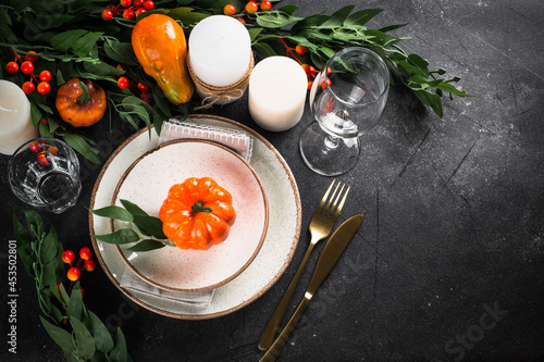 Autumn table setting with plate, cutlery, pumpkin and candles. Thanksgiving food festive dinner concept. Top view at black table. photo