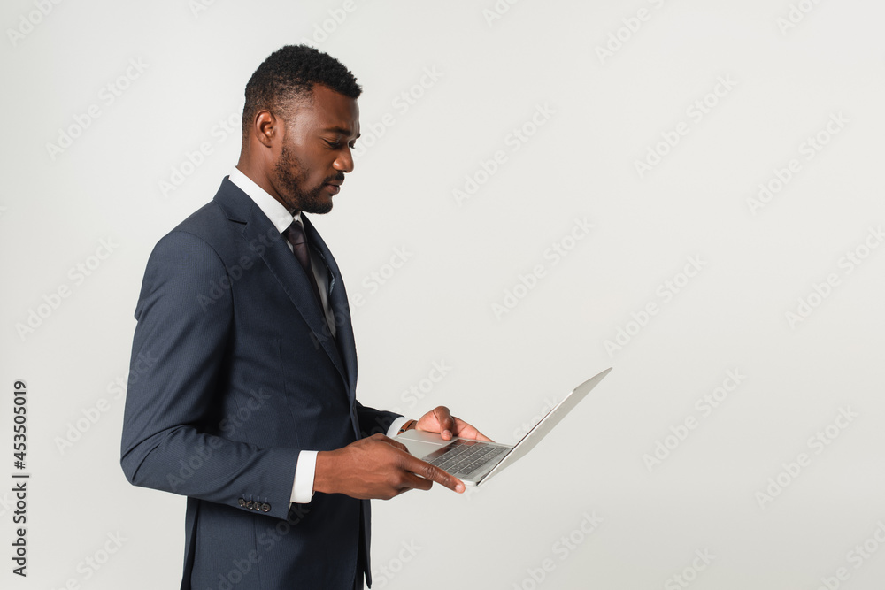 african american businessman in suit looking at laptop isolated on grey african american businessman in suit looking at laptop isolated on grey