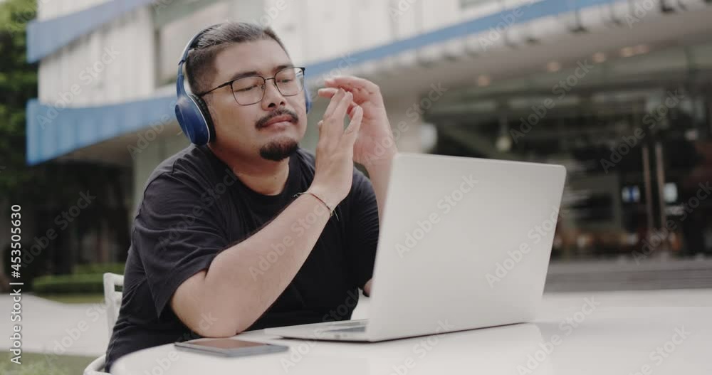 Asian Obese man wearing glasses, headphone to video call with laptop meeting outside. webinar with colleagues. using video conference app video call virtual communication. entertainment online Asian Obese man wearing glasses, headphone to video call with laptop meeting outside. webinar with colleagues. using video conference app video call virtual communication. entertainment online