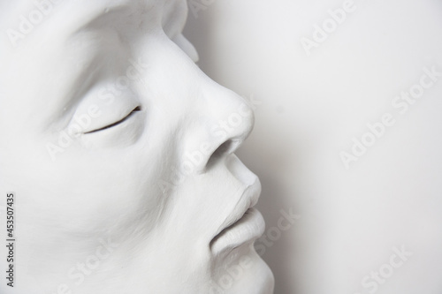 Portrait of a white face on a white background. Detail of sculpture with closed eyes.
