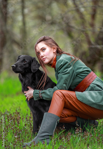 Portrait of young woman in country style clothes with black retriever dog in autumn forest