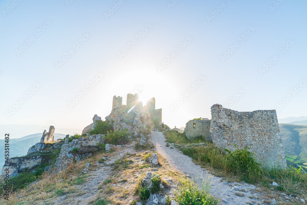 Castle ruins on mountain top at Rocca Calascio, italian travel destination, landmark in the Gran Sasso National Park, Abruzzo, Italy. Clear blue sky sun burst in backlight