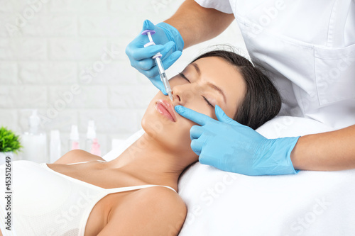Cosmetologist does injections for lips augmentation and anti wrinkle in the nasolabial folds of a beautiful woman. Women's cosmetology in the beauty salon.