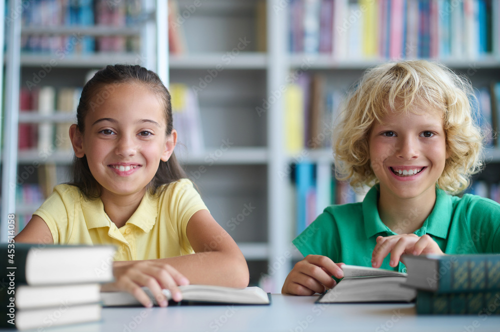 Two schoolchildren posing for the camera at the library desk Two schoolchildren posing for the camera at the library desk