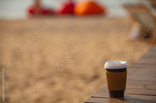 Disposable coffee cup on wooden background on the sandy beach