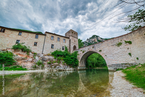 Dramatic sky over medieval village on river, San Vittore Frasassi, Marche, Italy. Romantic sky and clouds above mountains landscape, tourism destination. photo